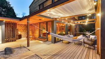 A modern house with a wooden deck, a hammock, and a barbecue area.