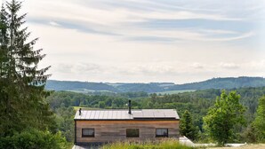 A wooden cabin with a metal roof, surrounded by dense forest and hills in the background. - Sauna House Zelené Údolí (Rabyně)