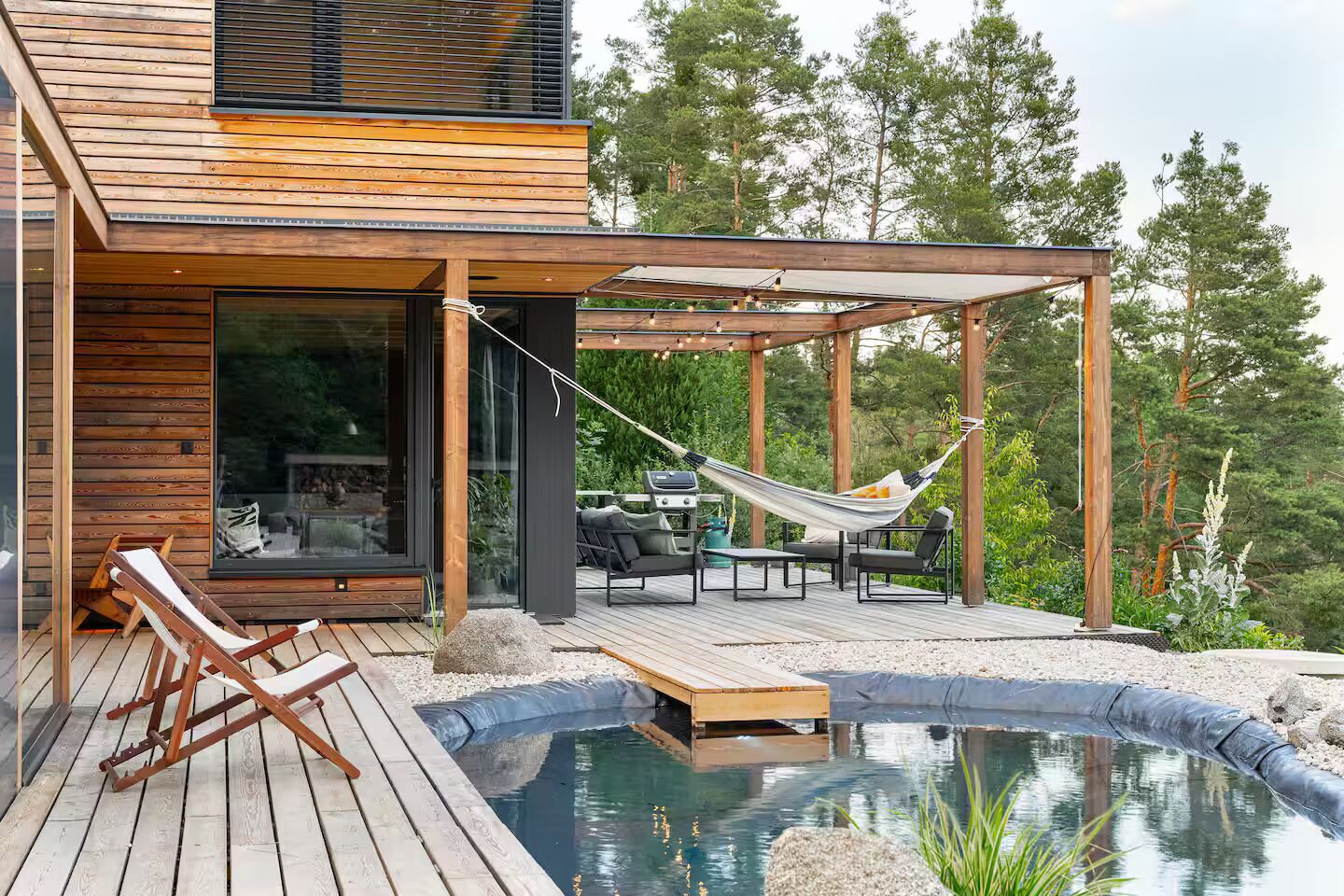 A modern outdoor deck with a pool, wooden furniture, and a hammock.