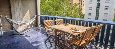 Ein Balkon mit Holztisch und -stühlen, einer Hängematte und Blick auf Gebäude und Bäume.