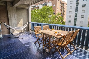 Uma varanda com mesa e cadeiras de madeira, uma rede e vista para edifícios e árvores.