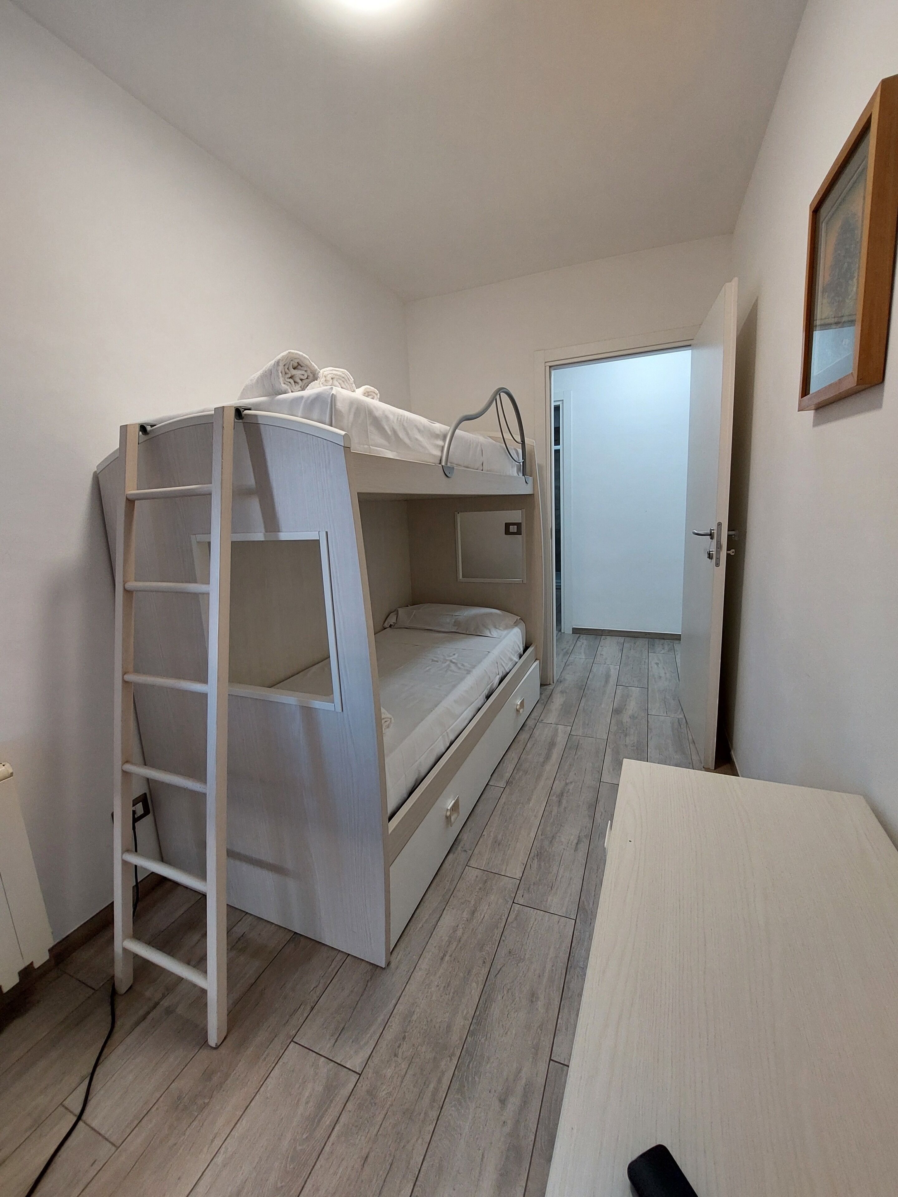 Cama litera con escalera, cama individual, escritorio y puerta que da a otra habitación.