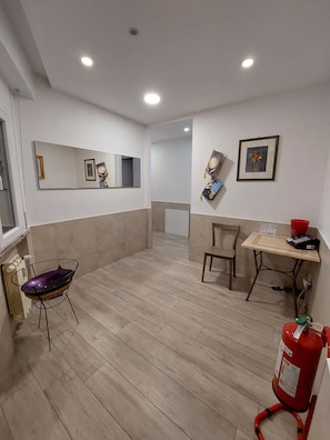 A room with a wooden floor, a chair, a small table with a red object on it, a fire extinguisher, and a mirror on the wall. - Il Bacio - Guest House (Perugia)