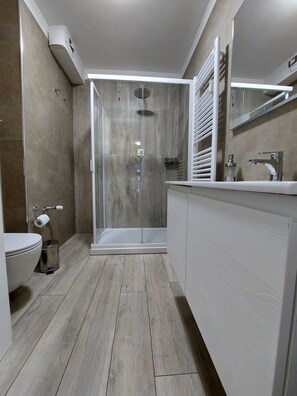 Um banheiro moderno com box de vidro, vaso sanitário e toucador com espelho.