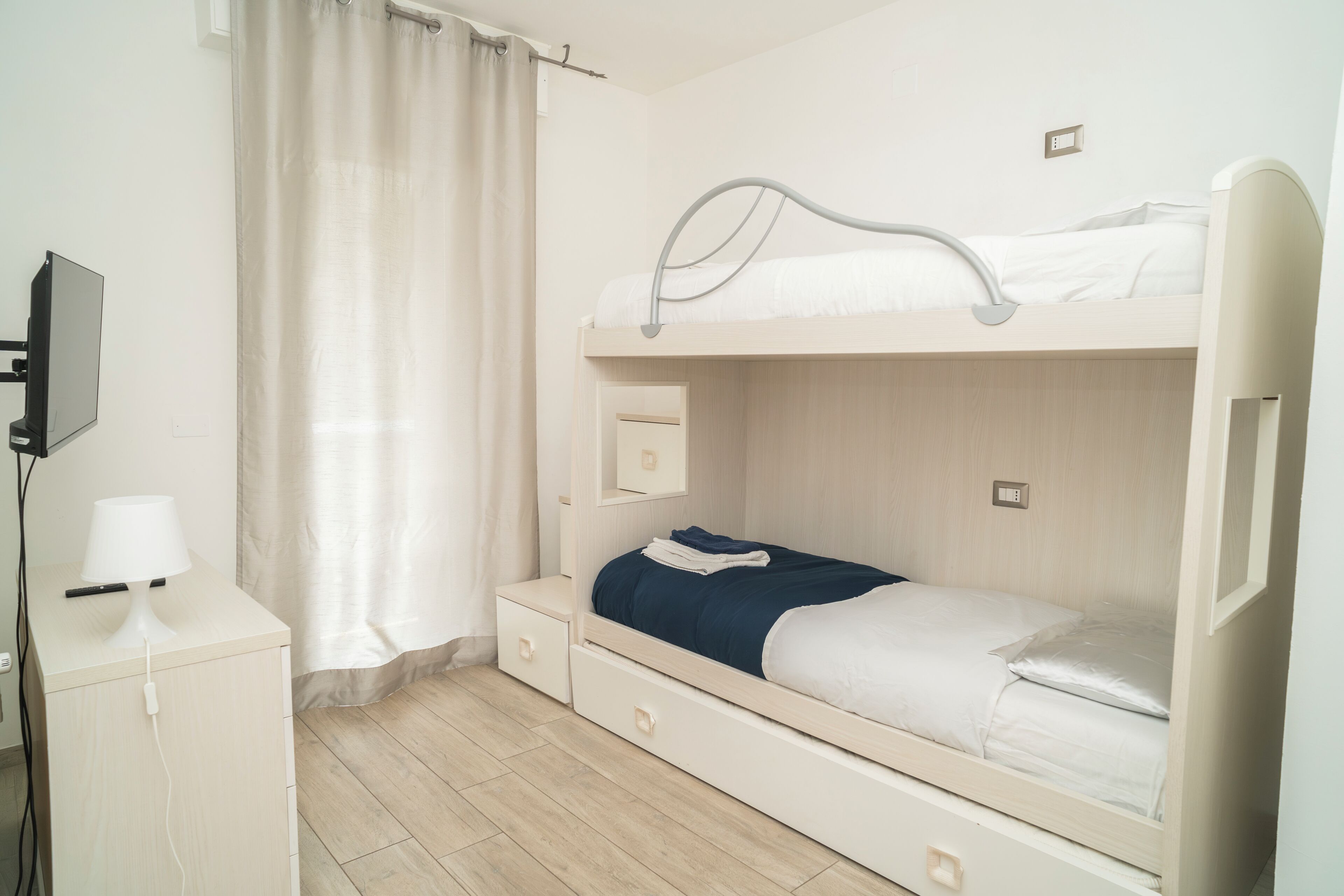 Un lit superposé avec un bureau et une chaise, une télévision et un rideau.