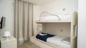 Una cama litera con escritorio, lámpara, cortina y televisor en la pared.