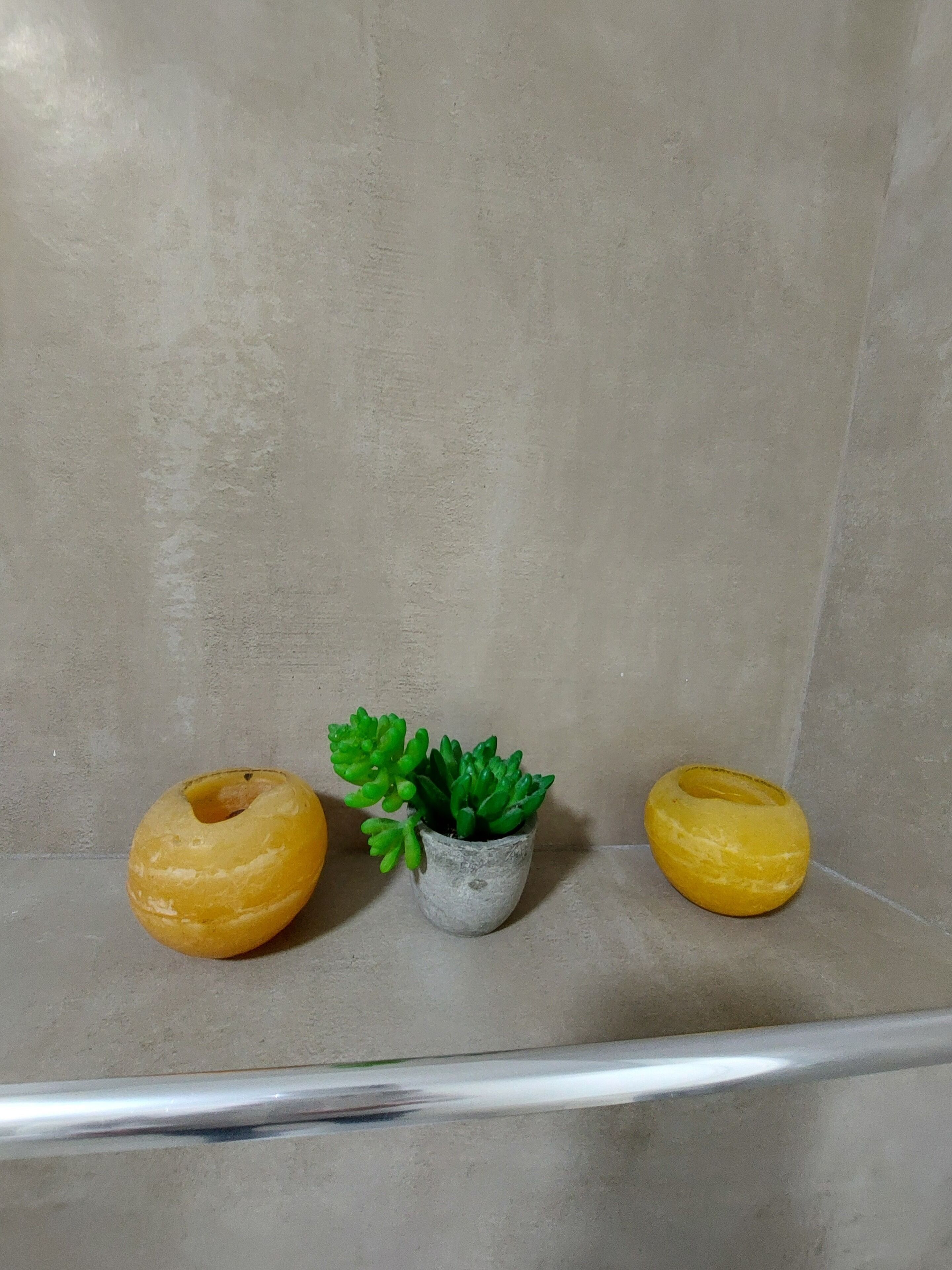 Une étagère sur laquelle se trouvent trois objets : une sphère jaune, une plante verte en pot et une autre sphère jaune.