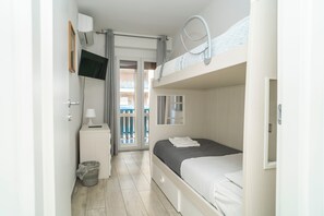 Quarto com uma cama beliche, mesa de cabeceira com abajur, TV fixada na parede e vista para a varanda.