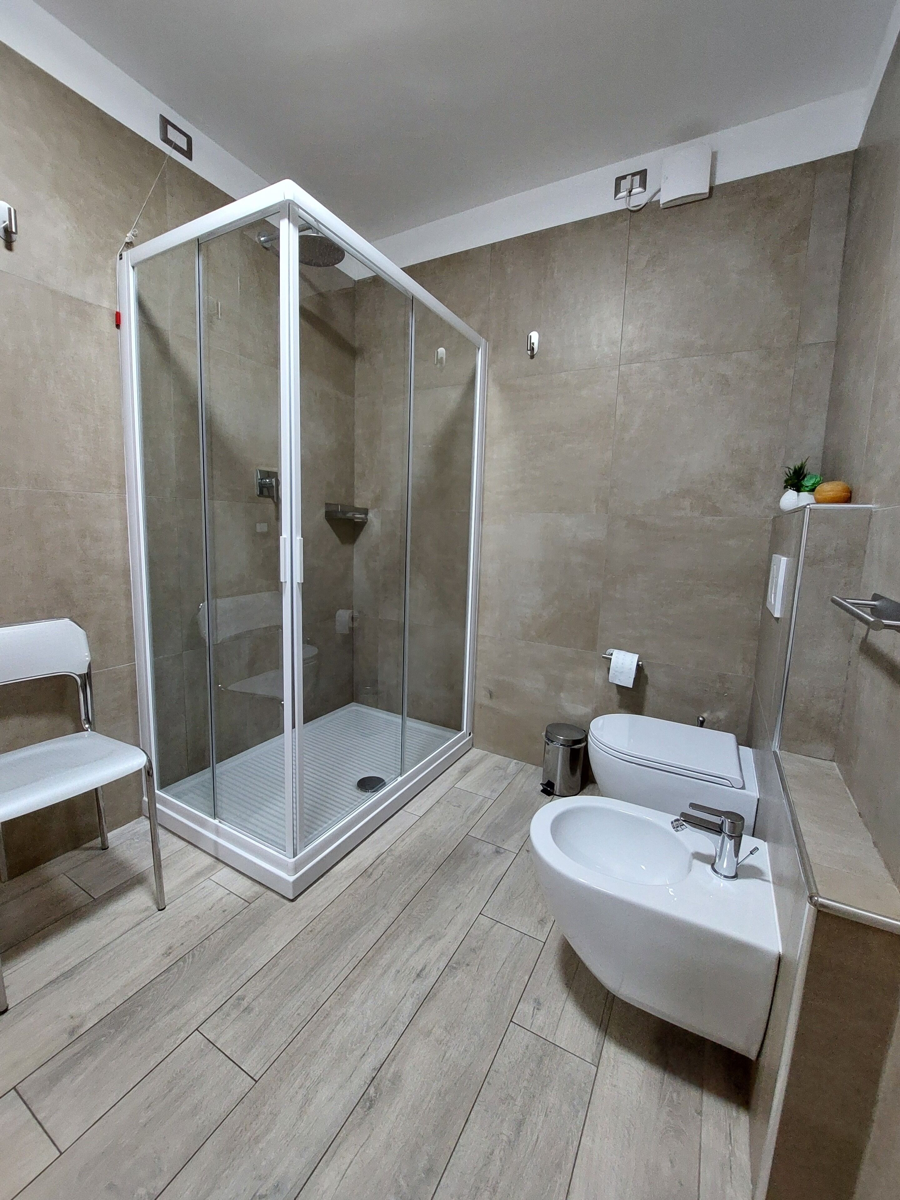 A modern bathroom with a glass-enclosed shower, a white sink, and a bench.