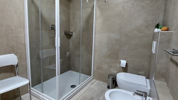 Ein modernes Badezimmer mit einer gläsernen Dusche, einem weißen Waschbecken und einer Sitzbank.
