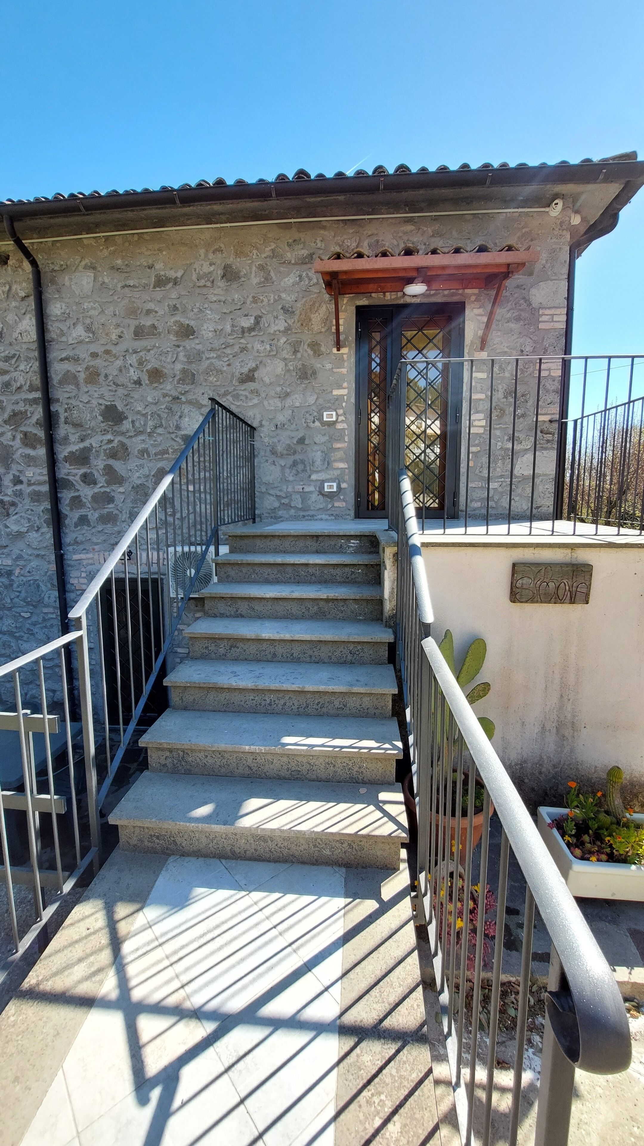A staircase leading to a stone building with a metal railing and a small garden area with plants.