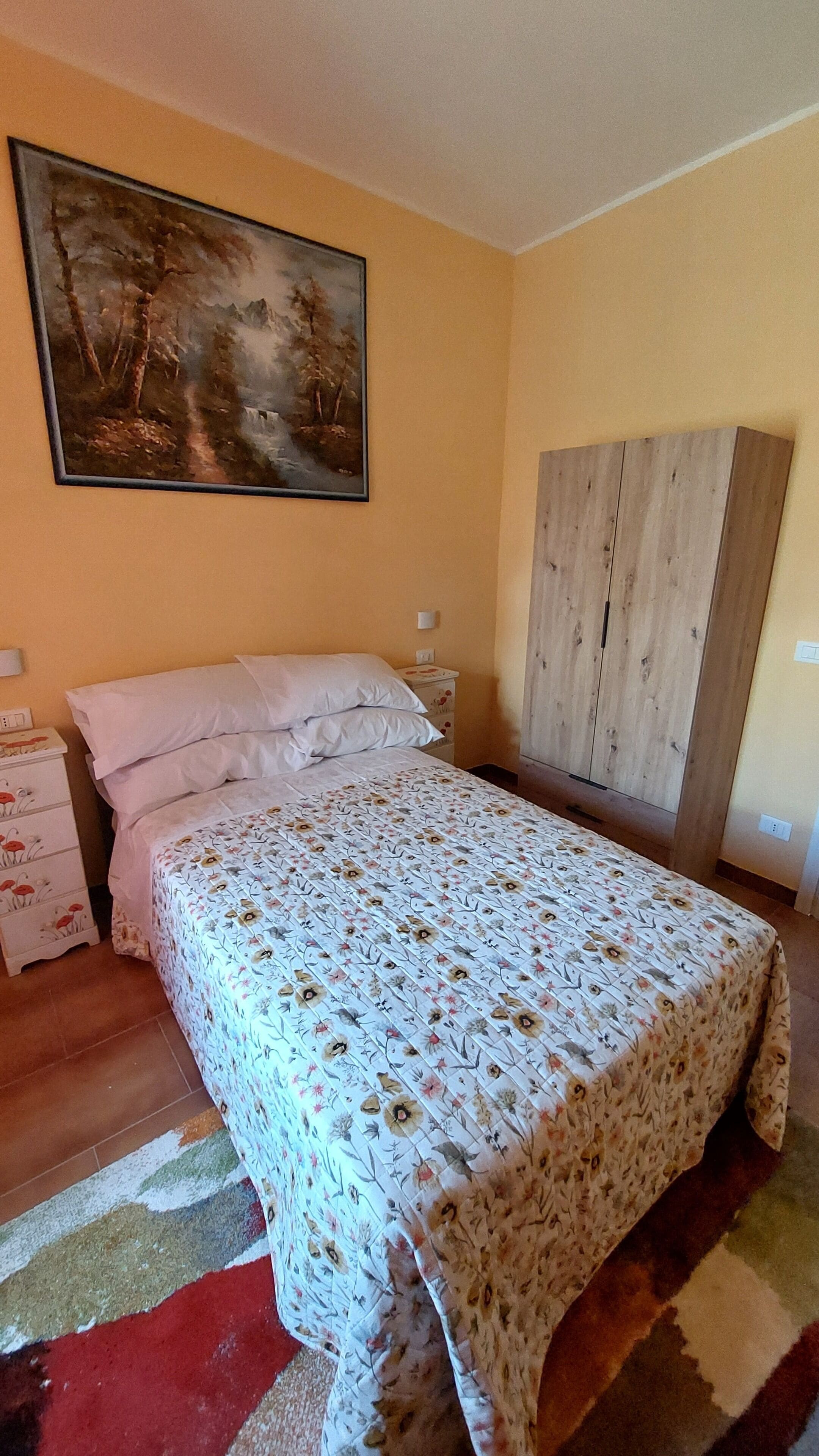 Un dormitorio con cama, mesita de noche, armario y un cuadro en la pared.