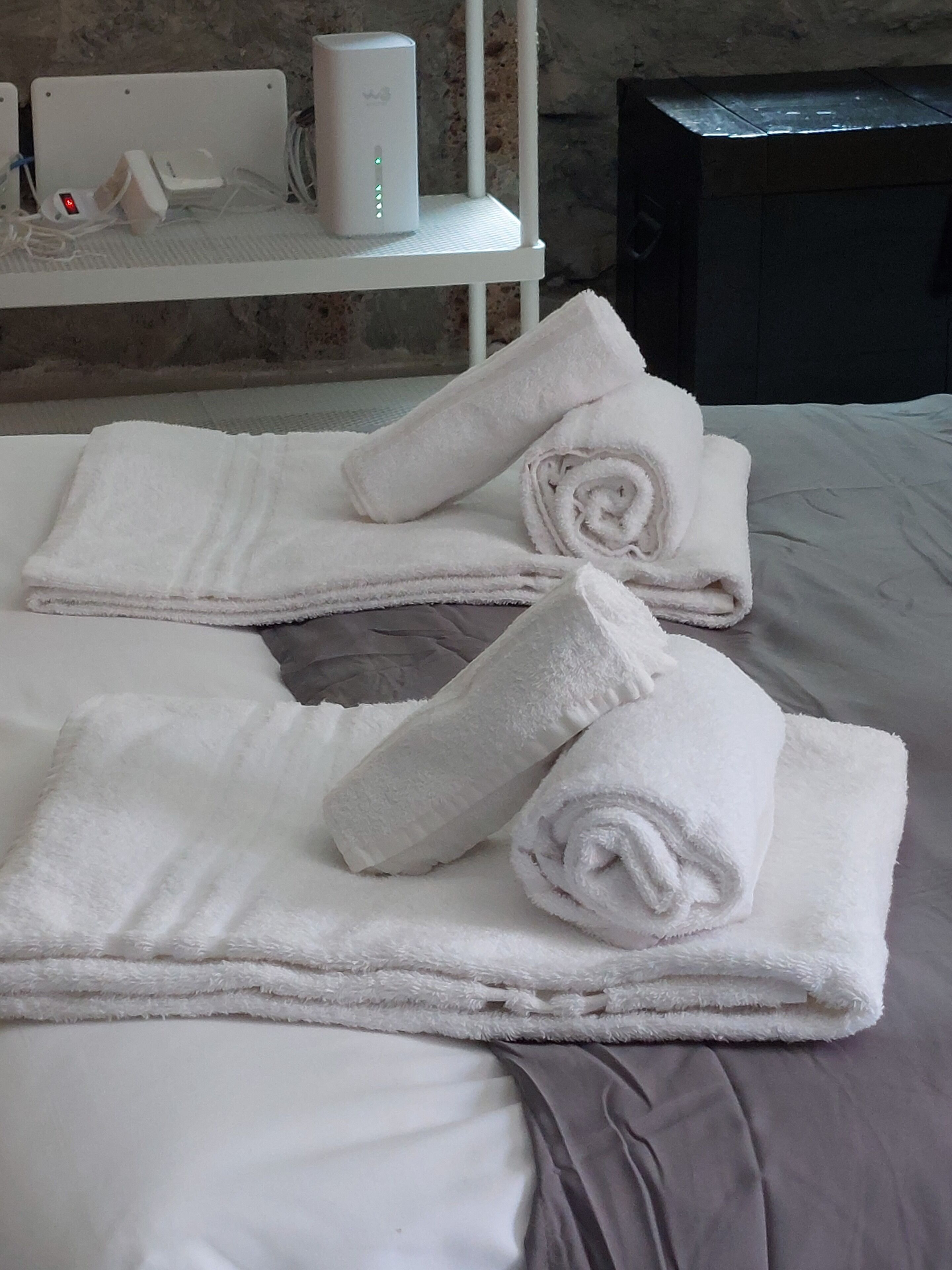 A neatly made bed with rolled white towels and a white shelf with various items.