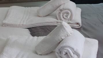 A neatly made bed with rolled white towels and a white shelf with various items.