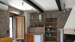Una cocina moderna con paredes de piedra, horno empotrado y un refrigerador pequeño. En la sala de estar, hay un sofá amarillo y un tapete estampado.