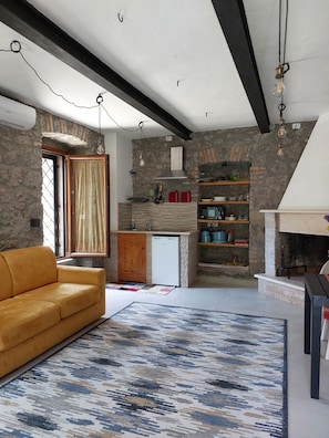 Una cocina moderna con paredes de piedra, horno empotrado y un refrigerador pequeño. En la sala de estar, hay un sofá amarillo y un tapete estampado.