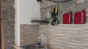 Una cocina con un lavamanos de acero inoxidable, armarios de madera, lavavajillas integrado y un salpicadero de pared de piedra.