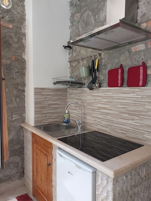 Una cocina con un lavamanos de acero inoxidable, armarios de madera, lavavajillas integrado y un salpicadero de pared de piedra.