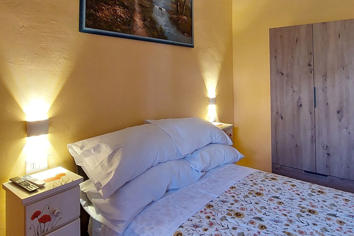Un dormitorio con cama, mesita de noche, cómoda, un cuadro y un armario de madera.