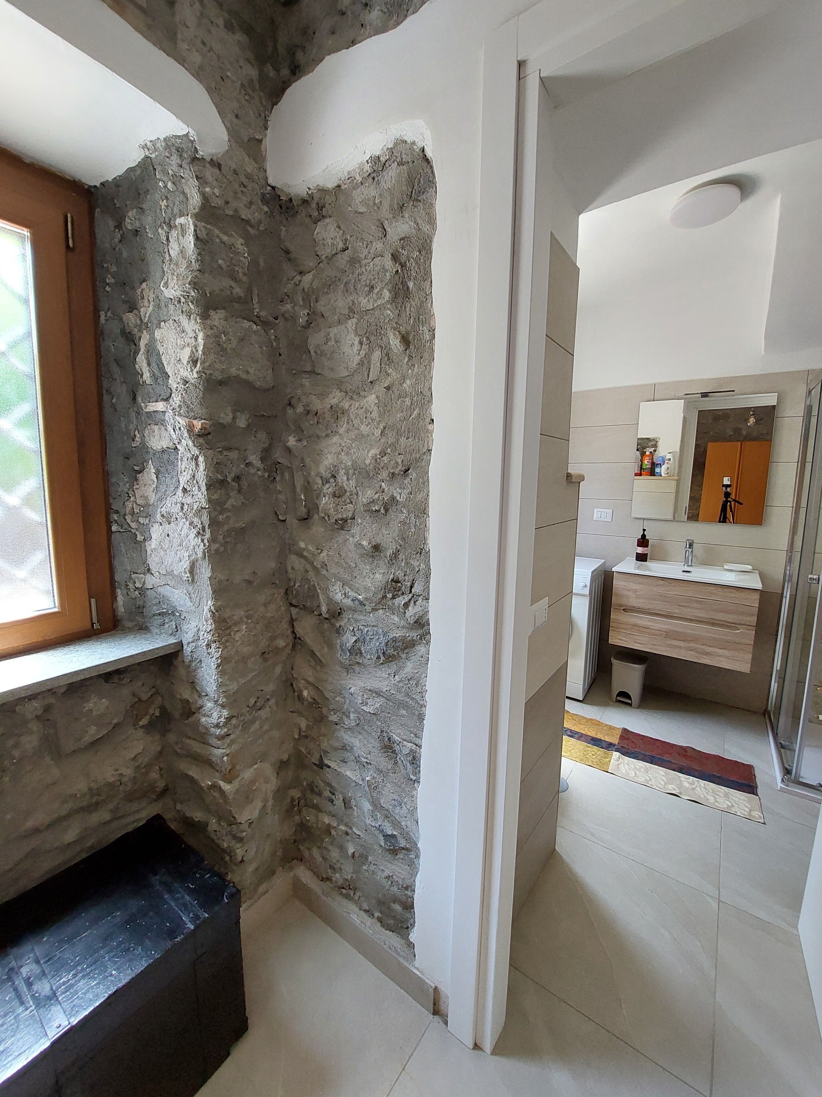 A bathroom with a stone wall, a wooden window, a tiled floor, and a modern sink with a mirror.