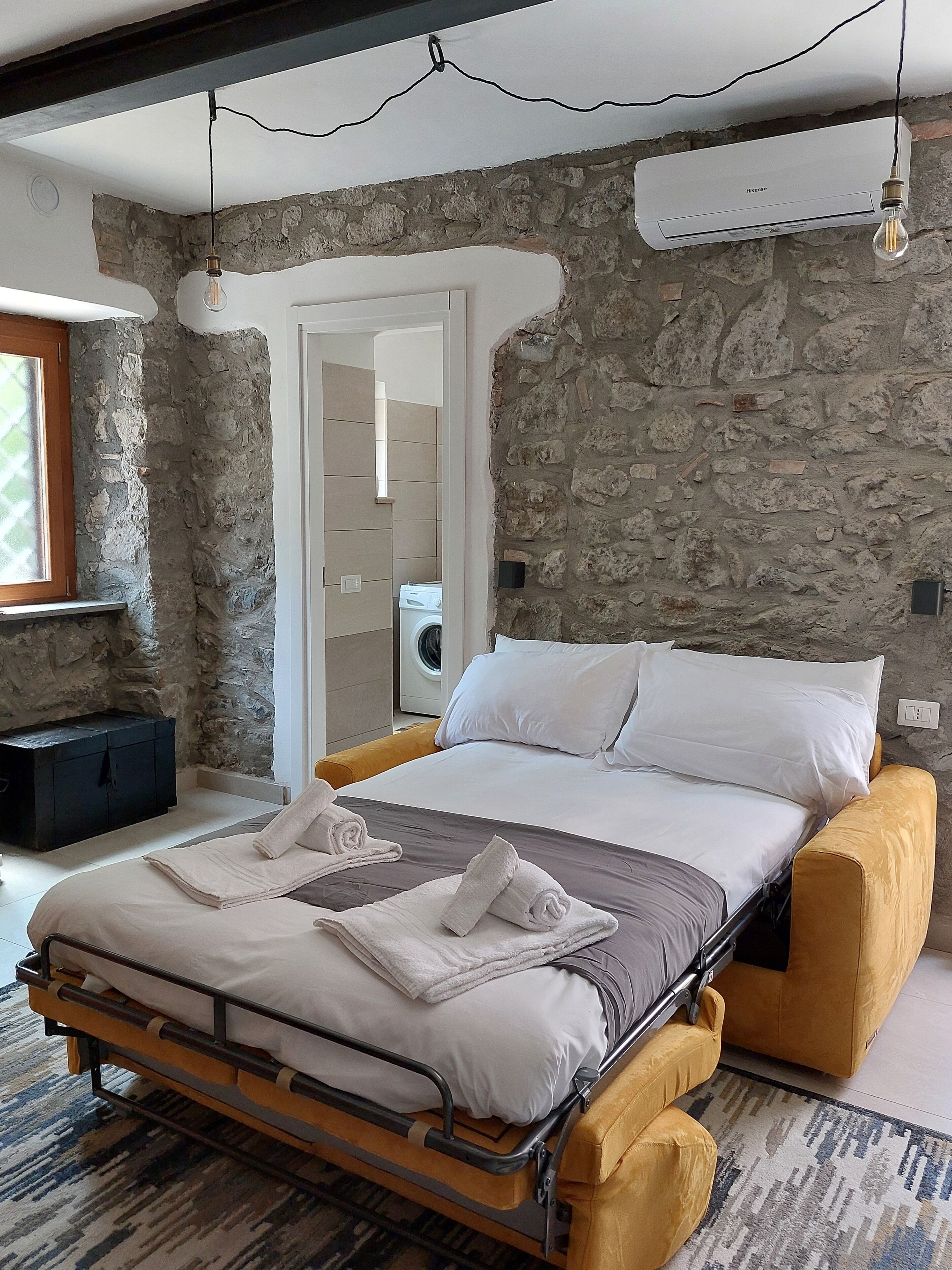 Un dormitorio con cama, lavadora y pared de piedra.