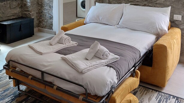 Un dormitorio con cama, lavadora y pared de piedra.