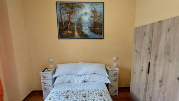 A bedroom with a bed, nightstands, a painting of a forest, and a wooden wardrobe.