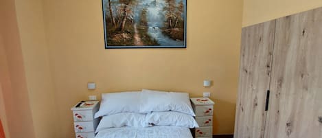 Un dormitorio con cama, mesitas de noche, un cuadro de un bosque y un armario de madera.