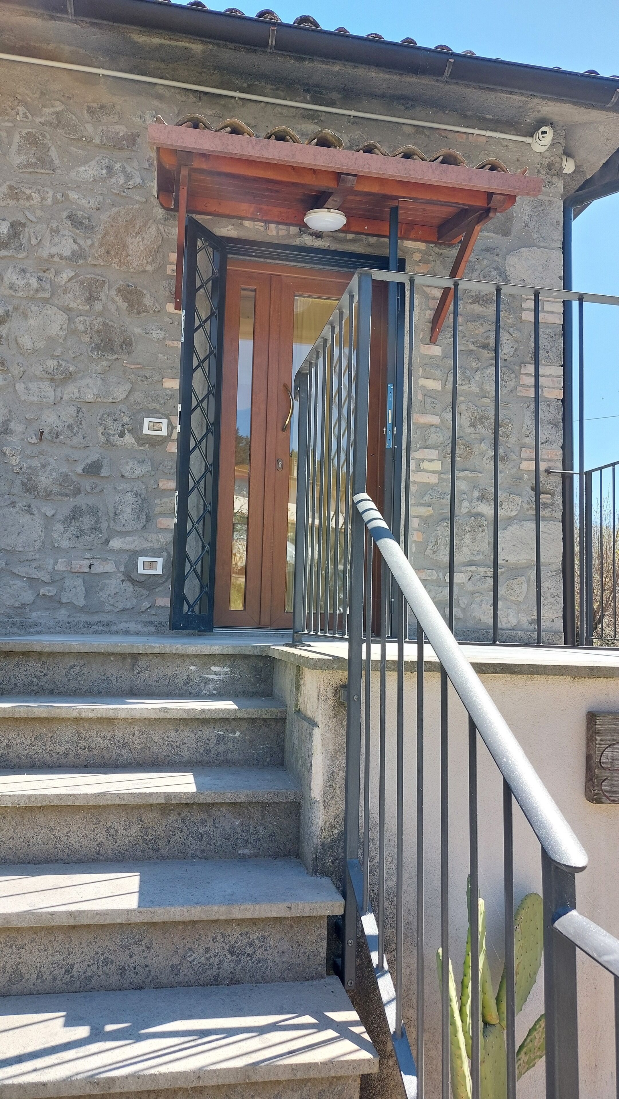 Un edificio de piedra con puerta de madera, barandilla metálica y un cactus al frente.