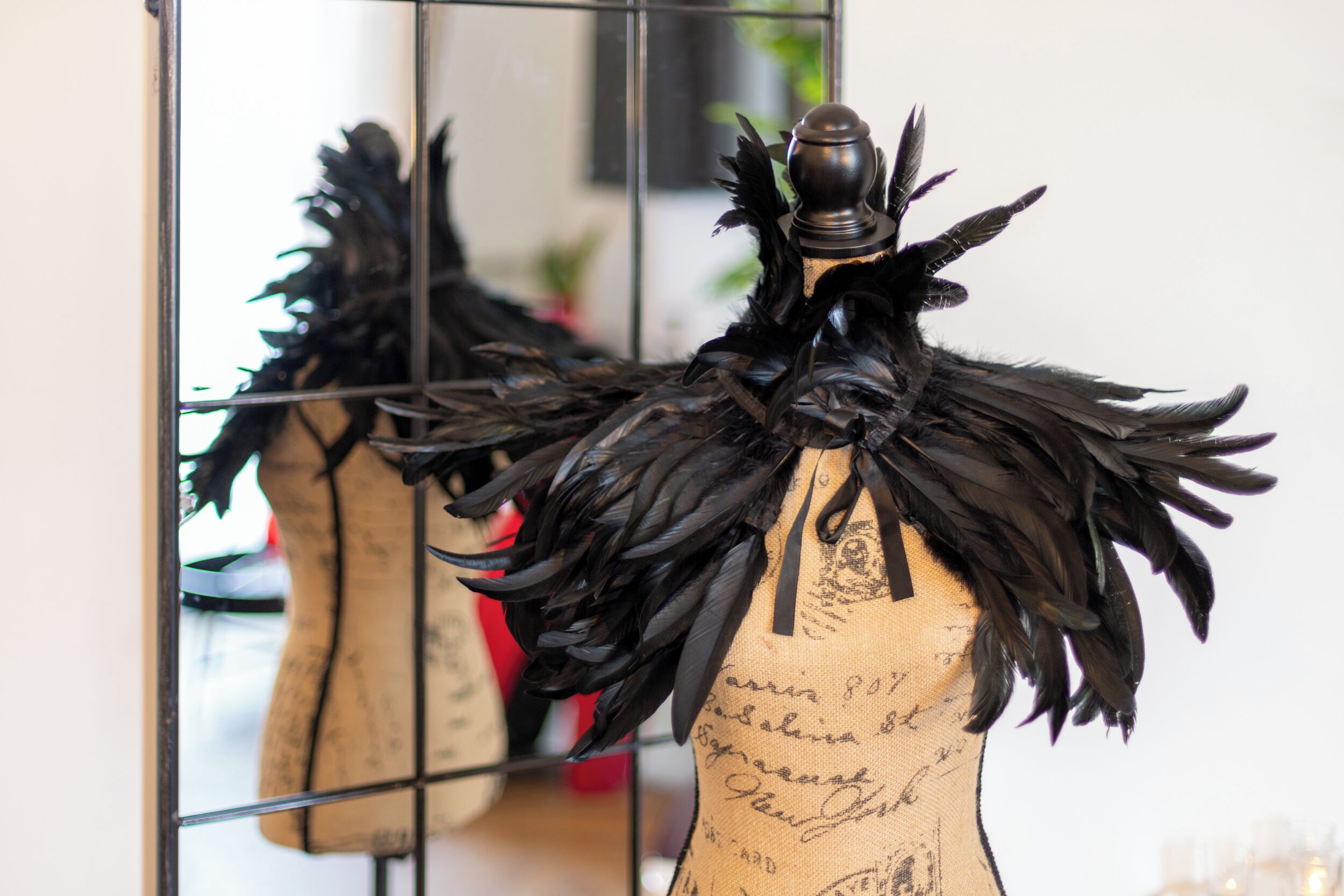 Un maniquí con una pieza de cabeza negra de plumas y una prenda color beige con texto escrito a mano.