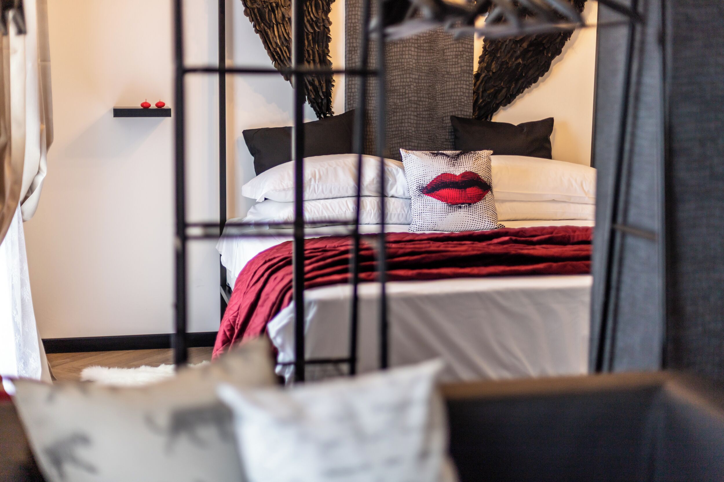Una camera da letto con un letto, cuscini, una coperta rossa e una mensola a parete con due oggetti rossi.
