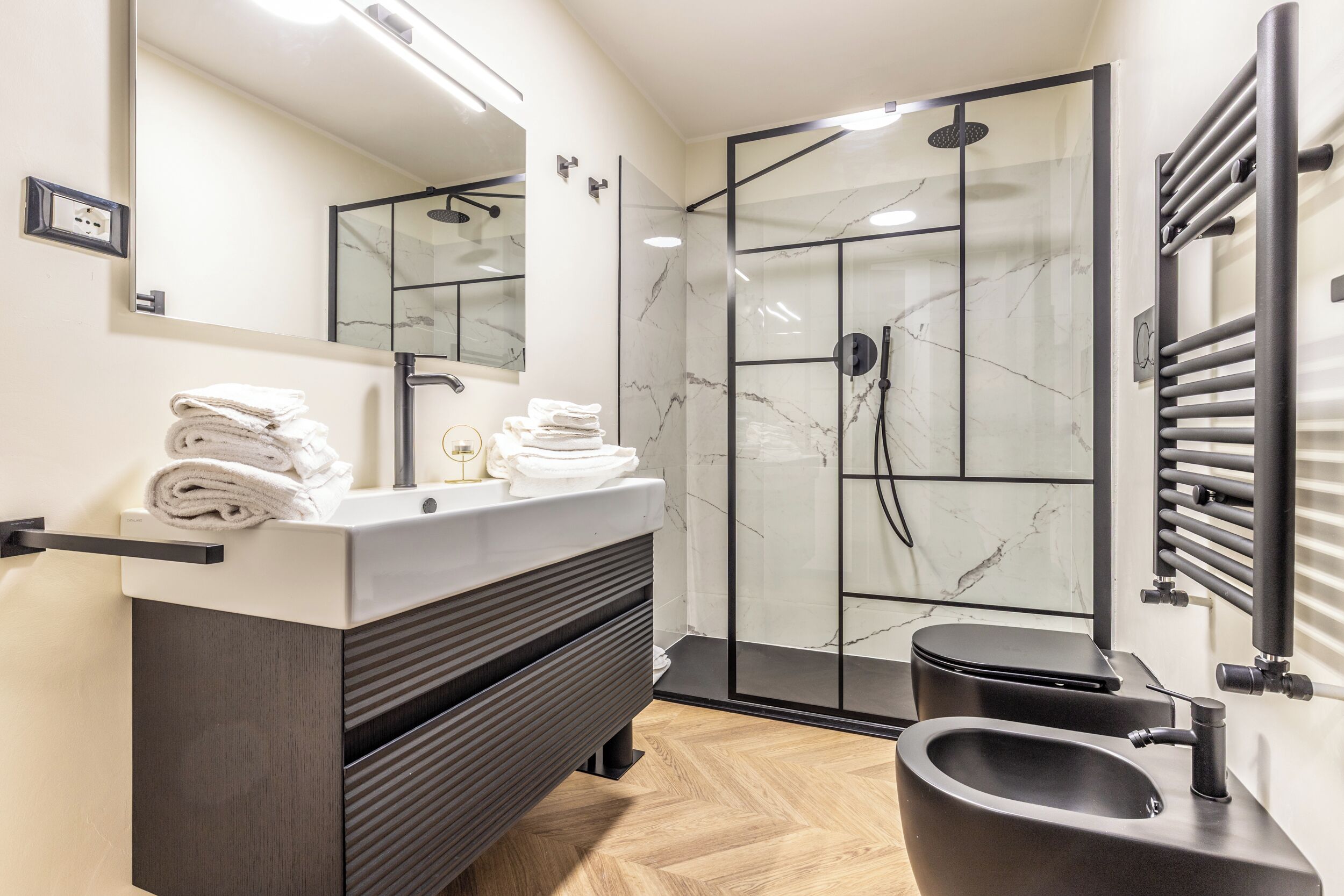 Une salle de bain moderne avec une douche à parois de verre, un meuble-lavabo doté d’un plan de travail en marbre et un lavabo noir.