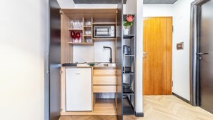 A compact kitchen with a built-in microwave, a sink, and a small refrigerator. There is a wooden cabinet with drawers and shelves above the counter. - Luxury Suite - Tentazioni Nascoste (Perugia)