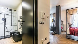 A modern hotel room with a shower, a bed with a red blanket, a phone, and a radiator. - Luxury Suite - Tentazioni Nascoste (Perugia)