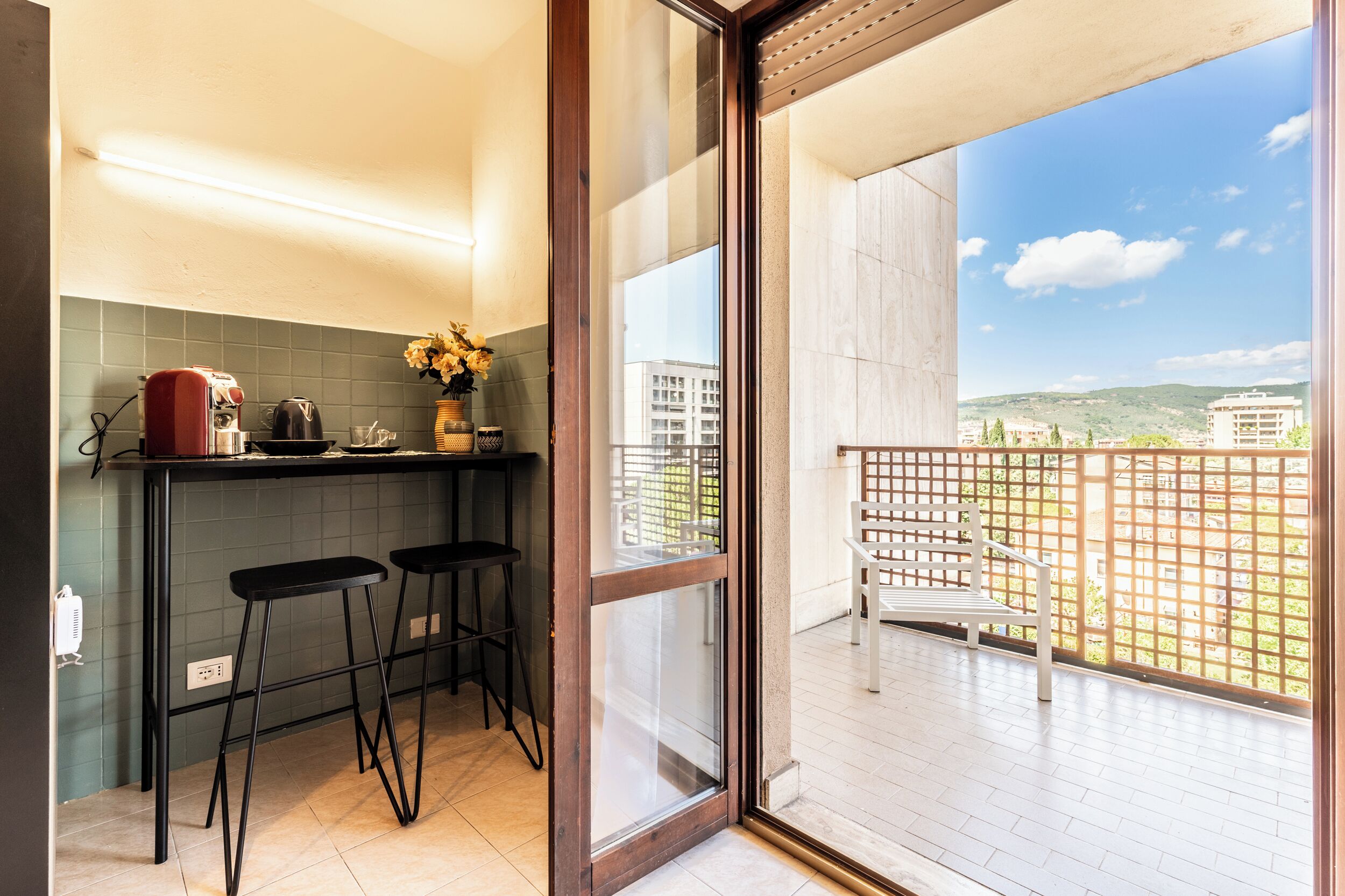 Una cocina con barra, dos taburetes y vistas a un balcón con cerramiento de madera y una banca.