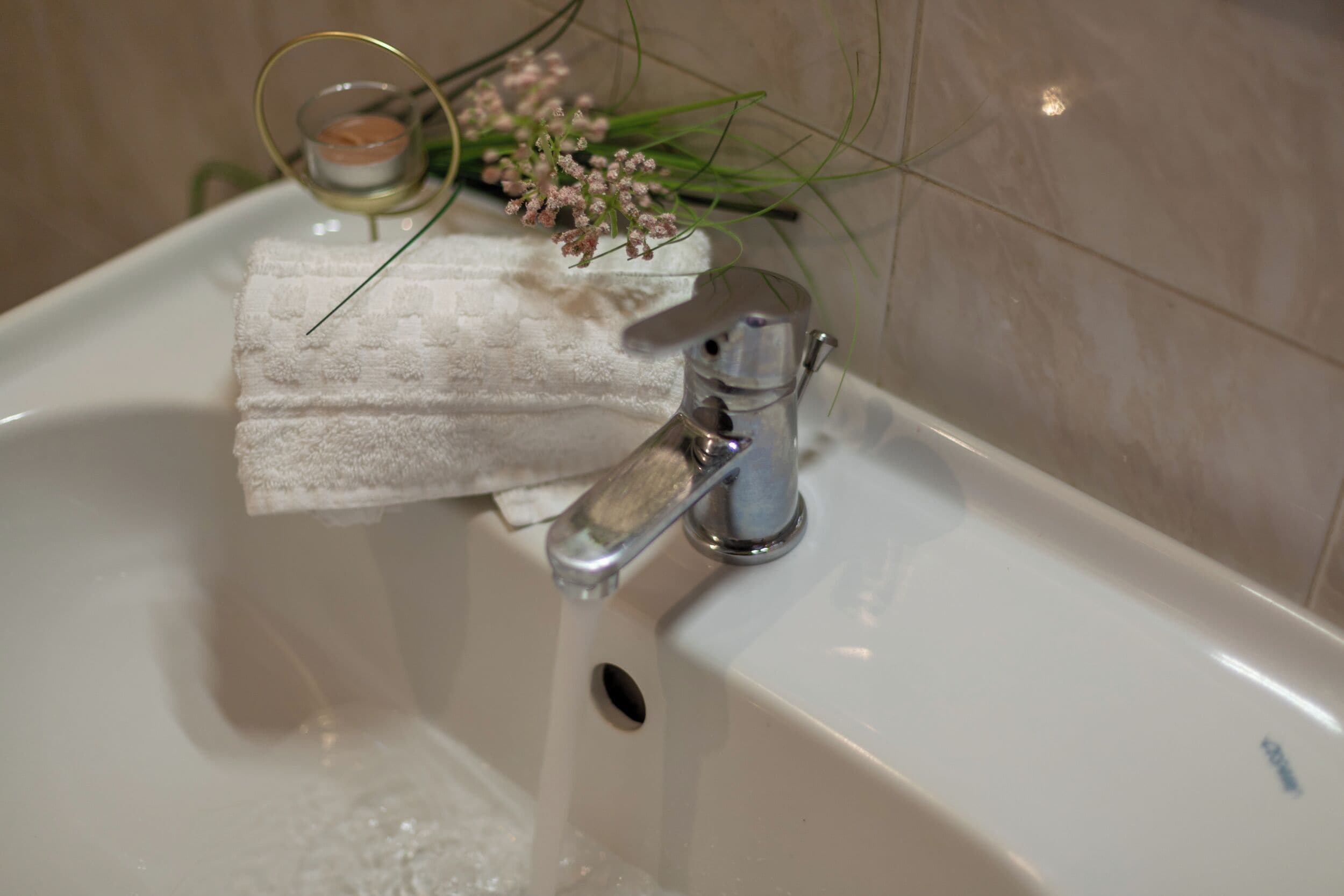 A bathroom sink with running water, a towel, and a small candle on the edge.