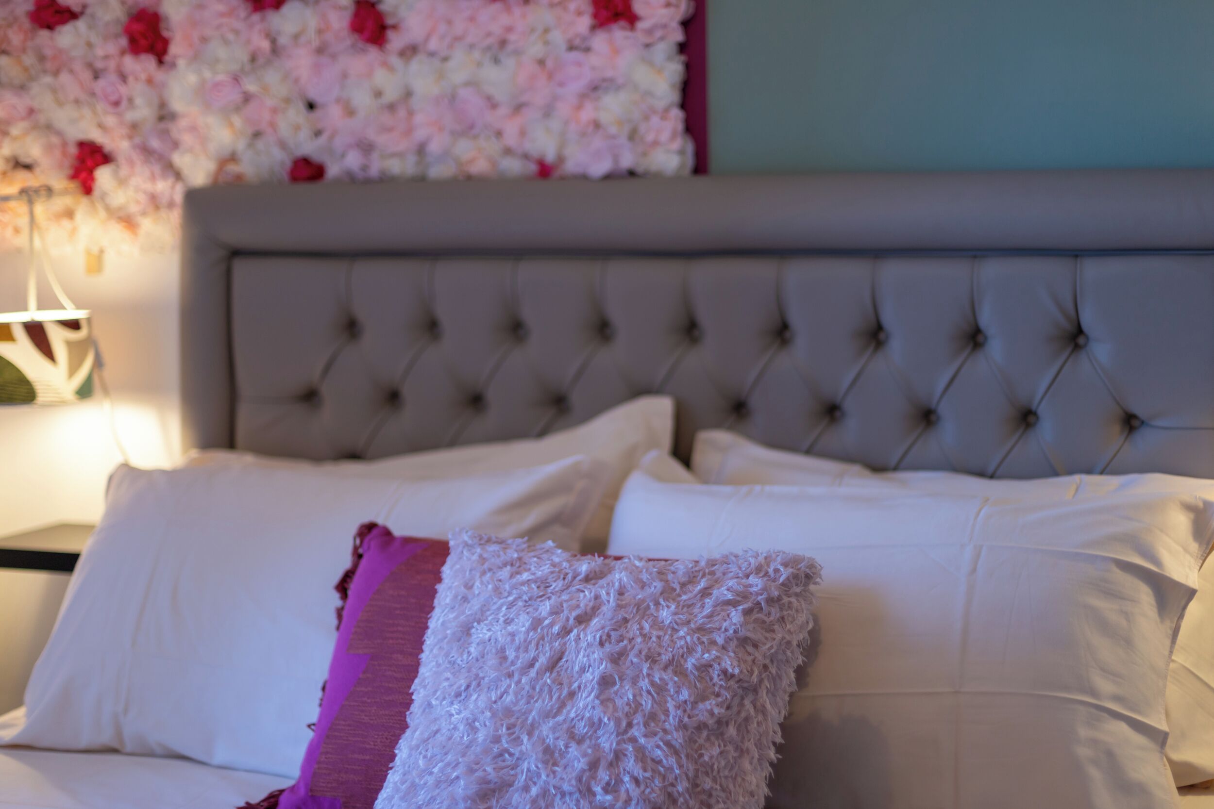 Un lit avec des oreillers blancs et roses, une tête de lit capitonnée et une décoration murale à motifs floraux.