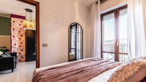 A bedroom with a bed, a window with curtains, a mirror, and a wall with a floral arrangement. - Luxury Suite - Tentazioni Romantiche (Perugia)