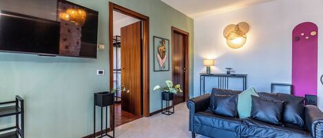 A living room with a black leather sofa, a flat-screen TV, a wooden door, and a wall-mounted light fixture.