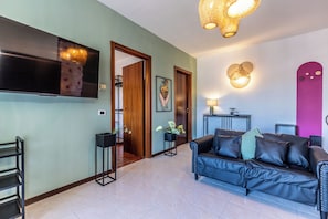 A living room with a black leather sofa, a flat-screen TV, a wooden door, and a wall-mounted light fixture. - Luxury Suite - Tentazioni Romantiche (Perugia)