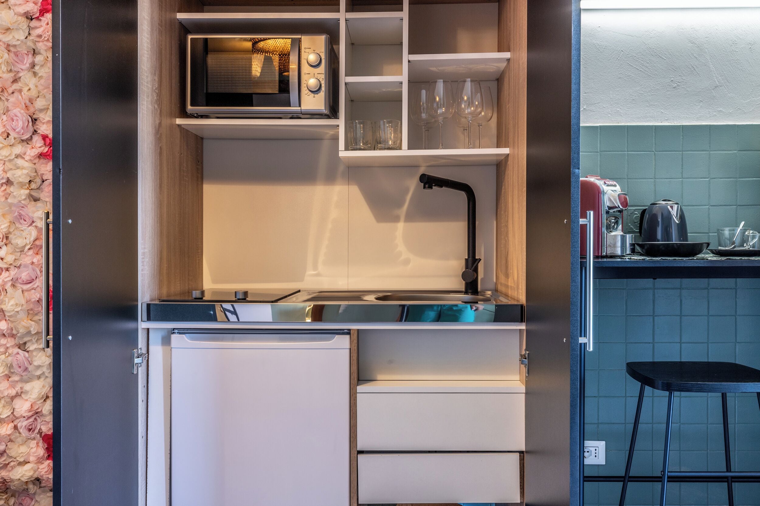 Uma cozinha compacta com micro-ondas, copos de vinho e pia.