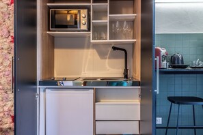 Uma cozinha compacta com micro-ondas, copos de vinho e pia.