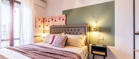 Une chambre à coucher avec un grand lit, une tête de lit, un arrangement floral fixé au mur, des lampes de chevet et une petite table de chevet.