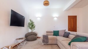 A living room with a beige sofa, a flat-screen TV, a small side table, and a wooden door. - A 15 Miglia da Roma (Riano)