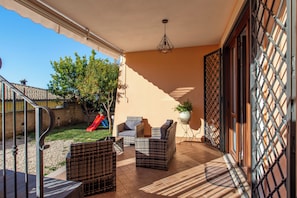 Un patio techado con mobiliario de mimbre, un tobogán rojo y vistas al jardín trasero.