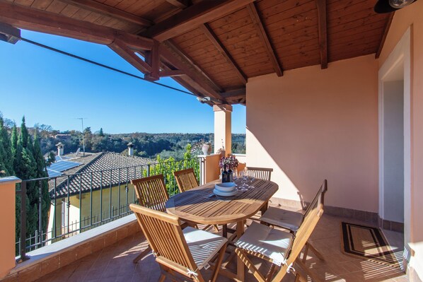 Un balcón de madera con una mesa y sillas, que ofrece una vista panorámica de casas y árboles.