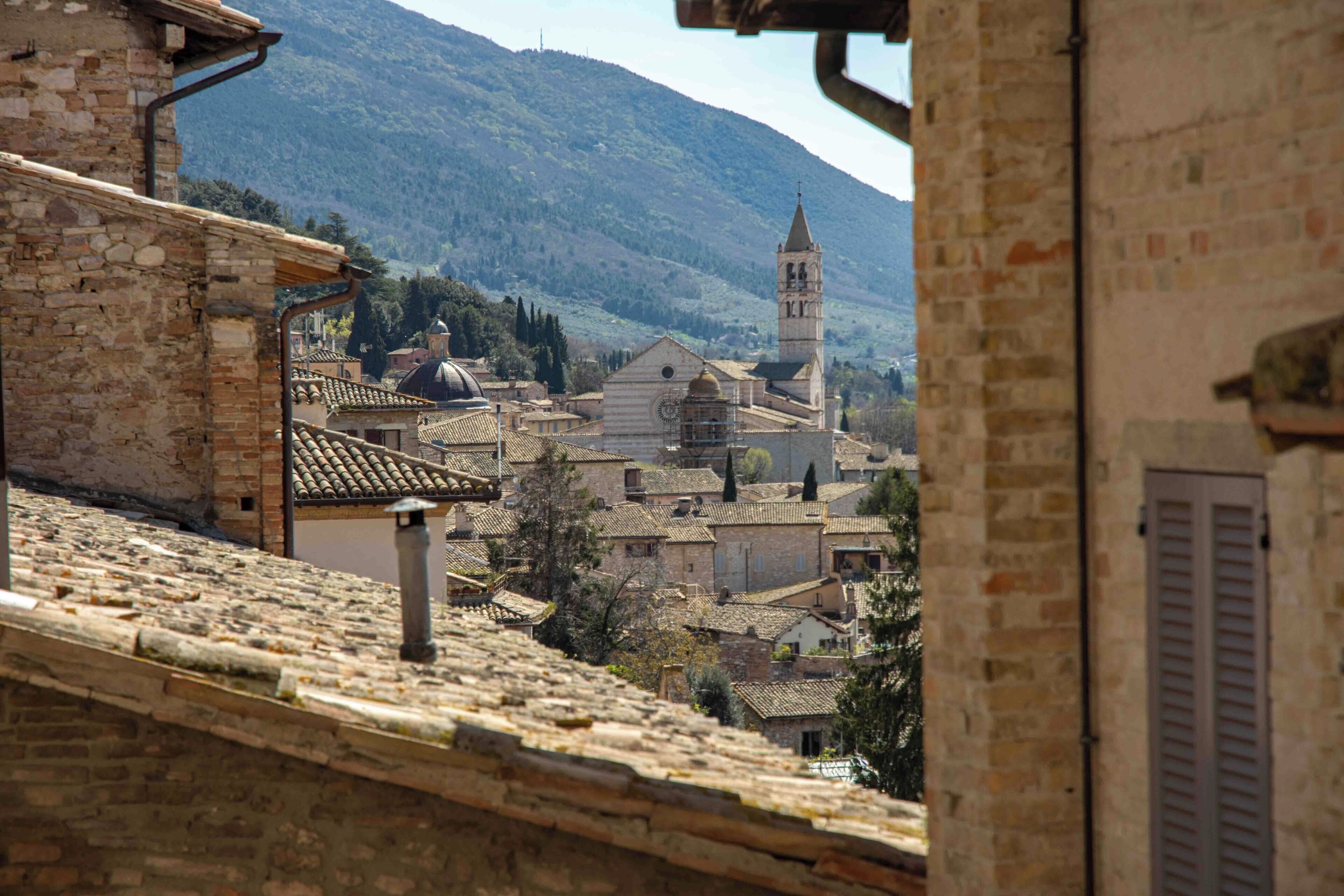 A historic town with stone buildings, a prominent church with a bell tower, and a mountainous backdrop.