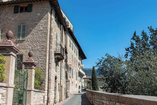 A stone building with a narrow street, a gate, and a tree.