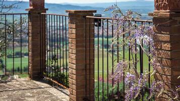 A gated entrance with a brick pillar and a metal gate, overlooking a green landscape with mountains in the distance.