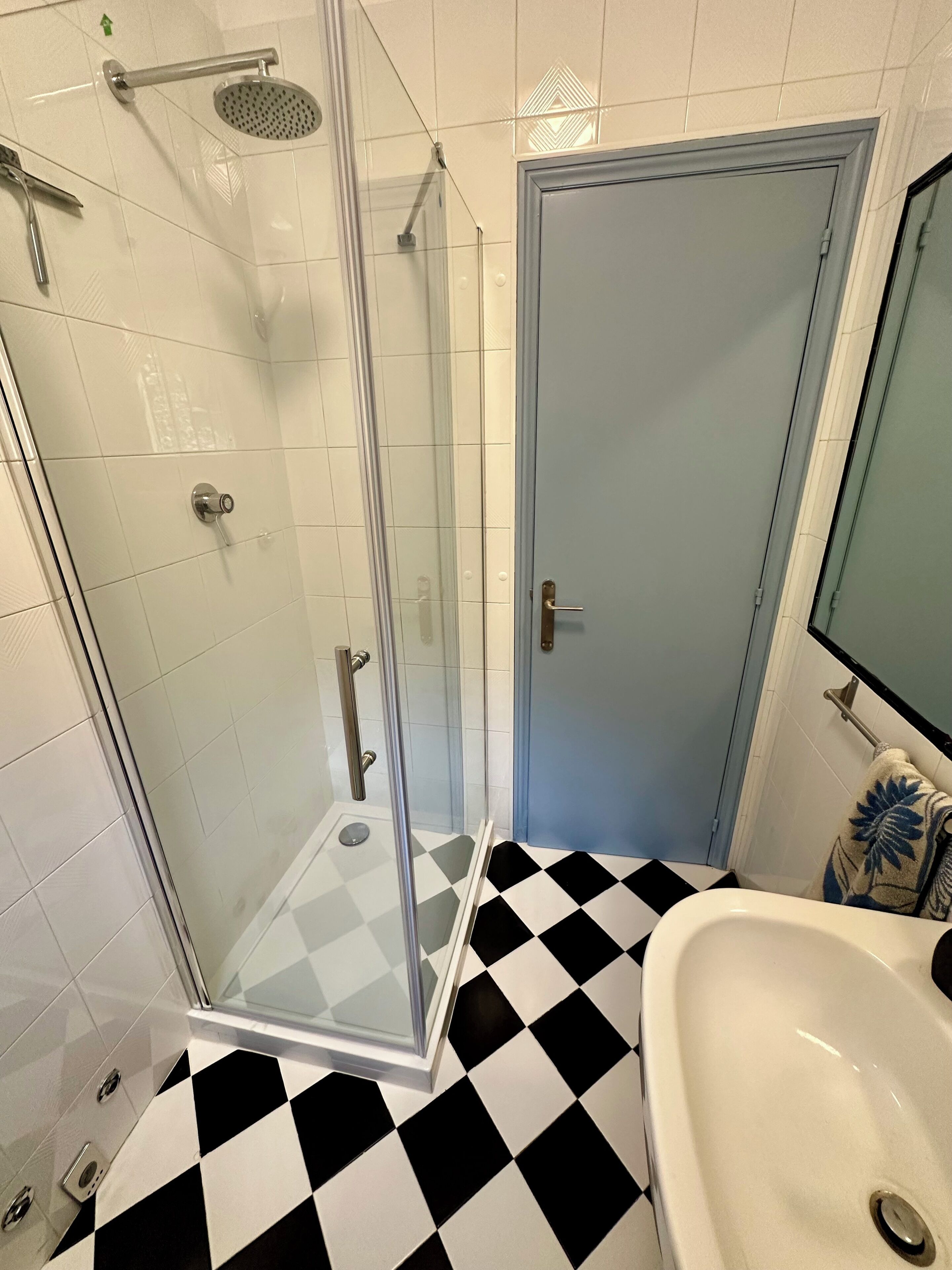 Un bagno con doccia vetrata, lavandino bianco e pavimento a scacchi.